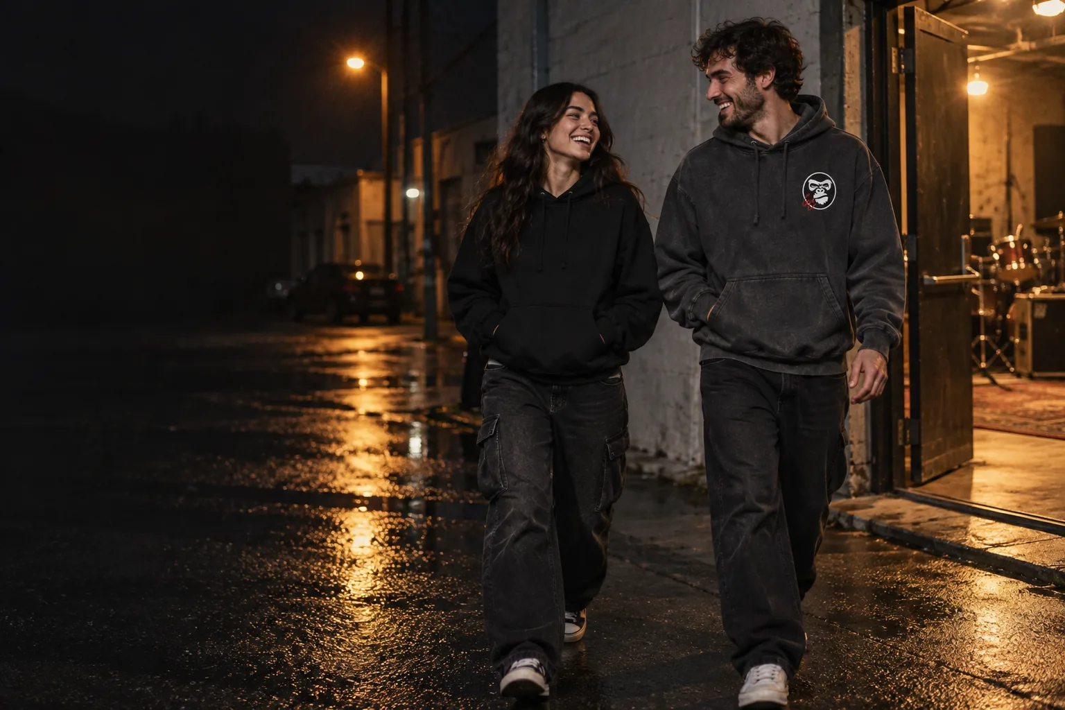 Illustrative campaign: two adult friends walking out of a studio into a night street, one in the GC Hoodie